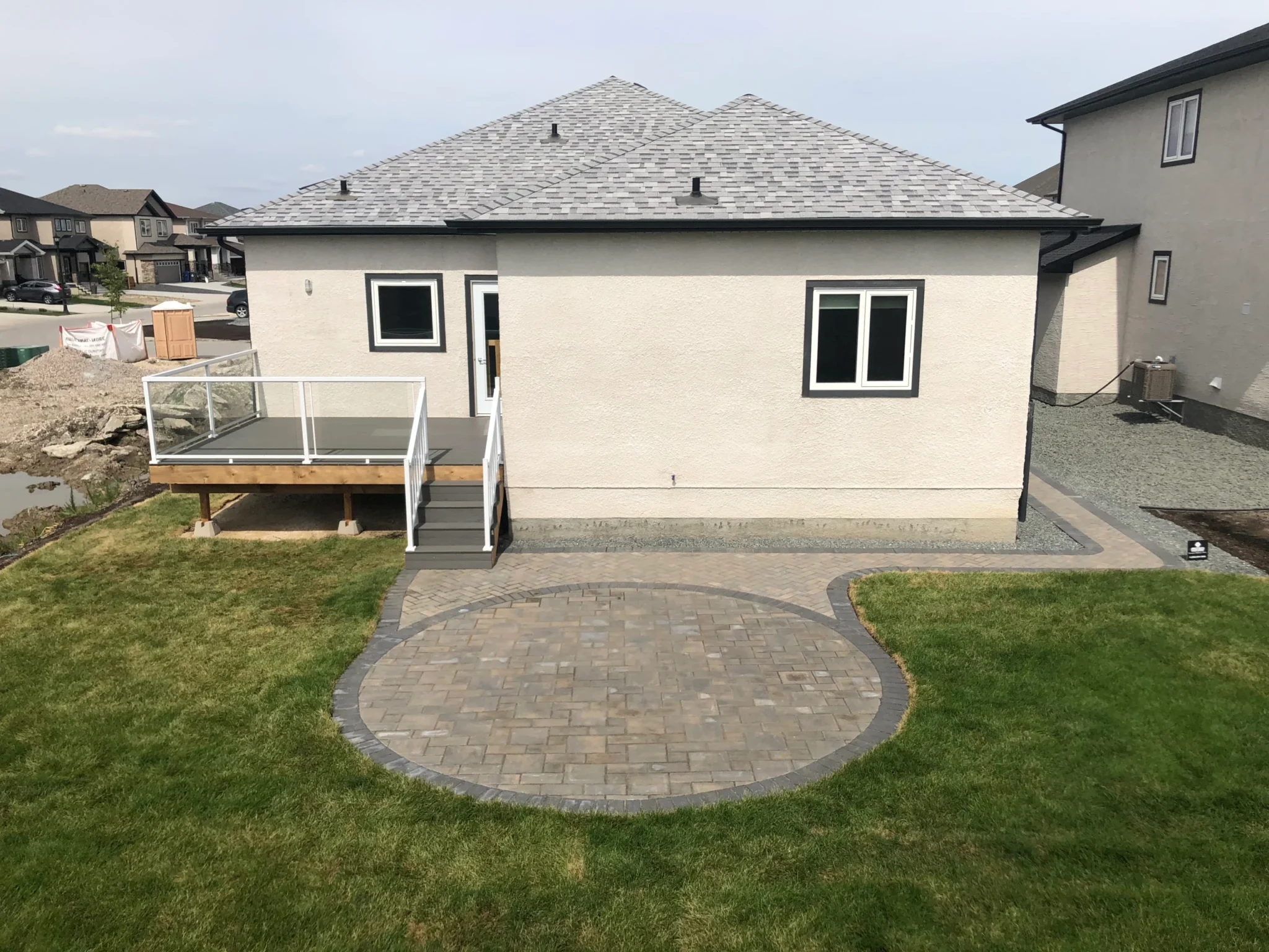 Custom landscaping backyard - Interlocking paver patio with circle inlay, composite deck with glass railing & sod