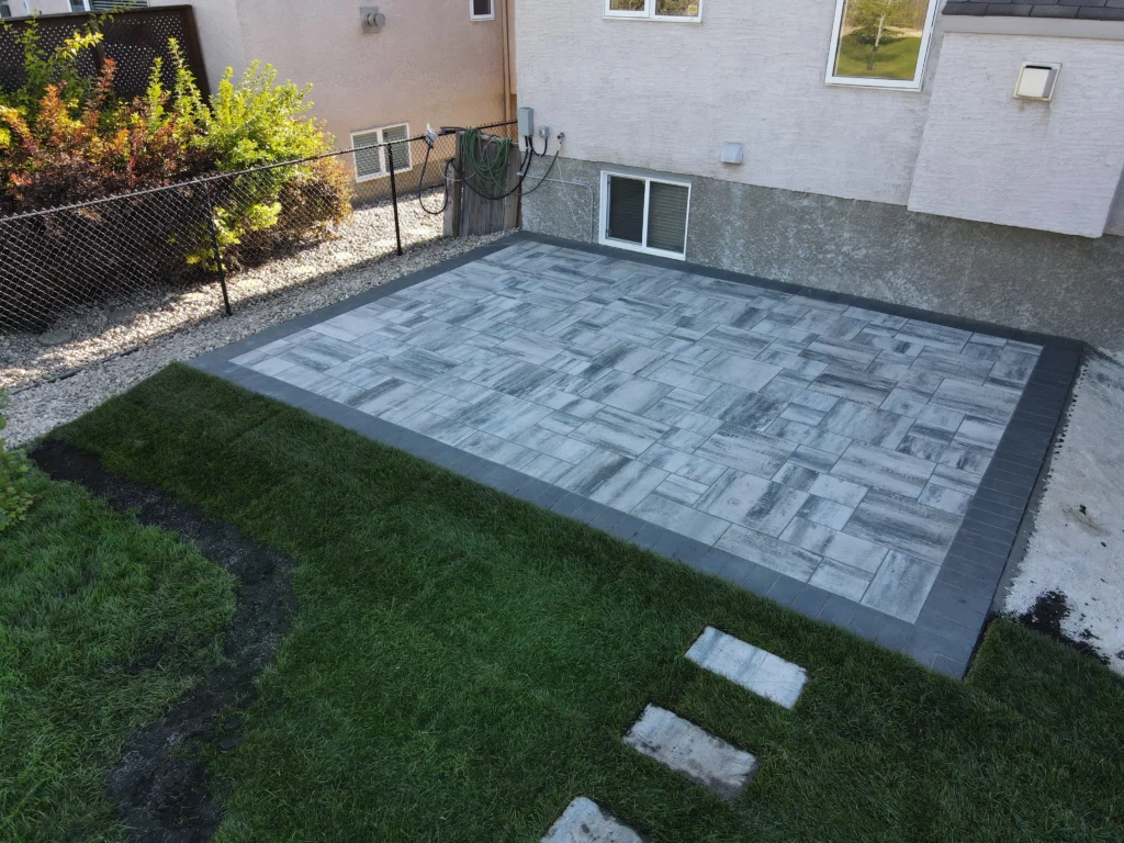 Genesis Interlocking & Custom Landscaping backyard hardscaping installation - Barkman Broadway slab patio installation with border & landscaping in Winnipeg Manitoba