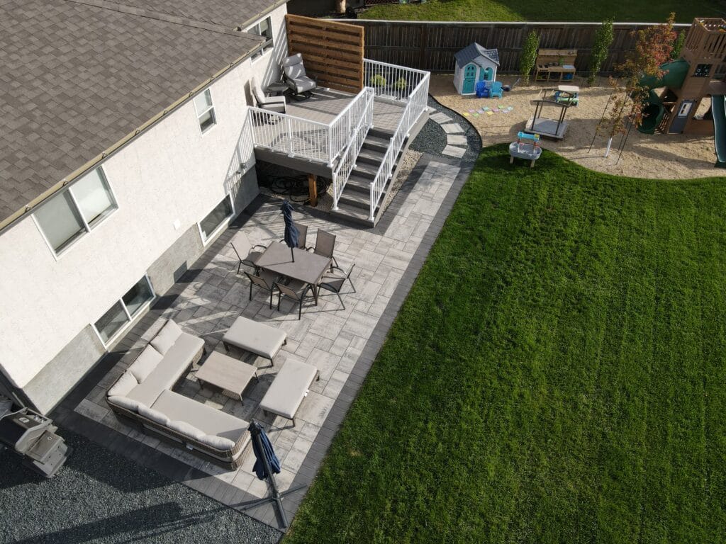 Backyard landscaping and hardscaping in Winnipeg manitoba featuring barkman broadway paver patio and stepping stones, composite deckorators deck with aluminum railing, play area & plants