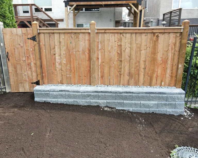 Allan Block retaining wall supporting a pressure treated fence completed by Genesis Interlocking & Custom Landscaping