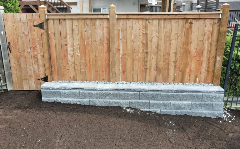 Allan Block retaining wall supporting a pressure treated fence completed by Genesis Interlocking & Custom Landscaping